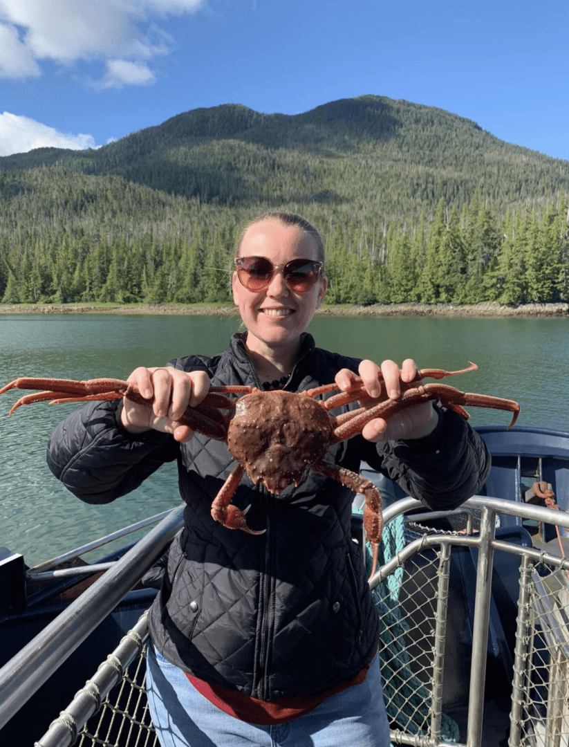 A woman holding up a crab on the back of a boat.